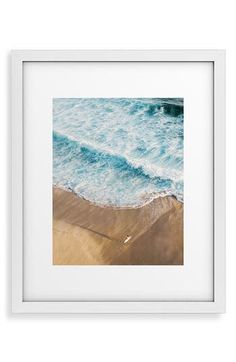 an ocean scene with waves crashing on the beach and sand in the foreground, framed in white