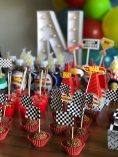 cupcakes are lined up on a table in front of balloons and race flags