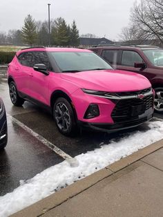 two pink cars parked in a parking lot with snow on the ground and trees behind them