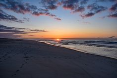 the sun is setting at the beach with footprints in the sand and people walking on the shore