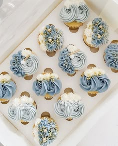 cupcakes with blue and white frosting are in a box on the table