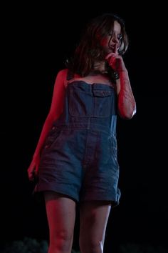 a woman in overalls standing on stage talking on her cell phone