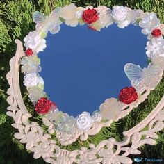 a heart shaped mirror sitting on top of a green tree covered in flowers and butterflies