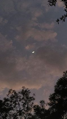 the moon is seen through the clouds in the sky above some tree tops at dusk