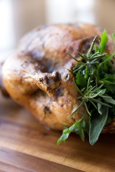 a close up of a chicken on a cutting board with leaves and herbs around it