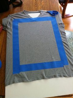 a t - shirt is being made on the floor with blue tape and some scissors