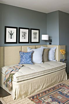 a day bed with pillows and pictures on the wall in a room that has blue walls