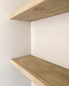 two wooden shelves on the wall with white walls in the background and one shelf is empty