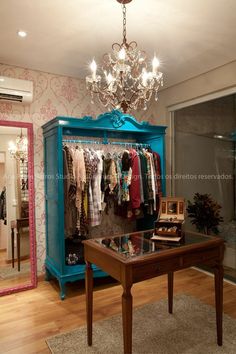 a blue armoire with clothes on hangers and a chandelier hanging from the ceiling