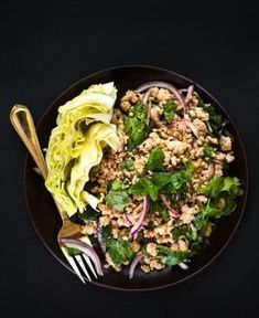 a black plate topped with lettuce and meat next to a fork on a table