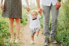 a little boy walking down a dirt road holding hands with his parents