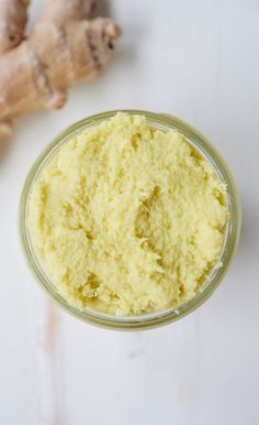 a glass jar filled with yellow colored powder next to ginger root on a white surface