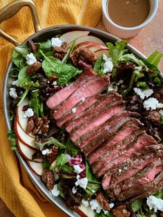 a steak salad with apples and feta cheese in a bowl next to a cup of coffee