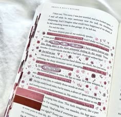 an open book with pink and red writing on it's pages, sitting on a white sheet