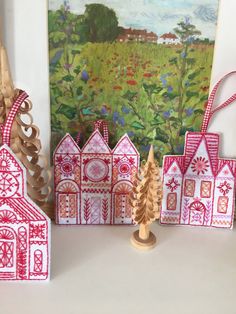 three handmade houses are sitting on a table next to a painting and some scissors