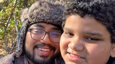 two men are posing for the camera with one wearing a winter hat and the other looking at the camera