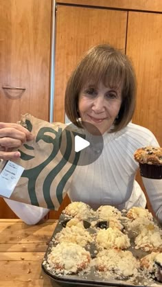 a woman sitting at a table with some cupcakes and muffins in front of her