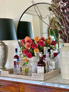 a table topped with bottles and vases filled with flowers sitting on top of a wooden dresser