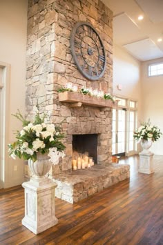 a stone fireplace with candles and flowers in front of it on a hard wood floor