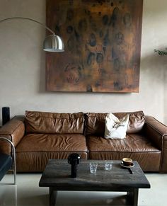 a living room with a brown leather couch and coffee table in front of a large painting