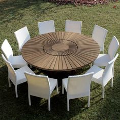 a round wooden table with white chairs around it on the grass in front of some trees