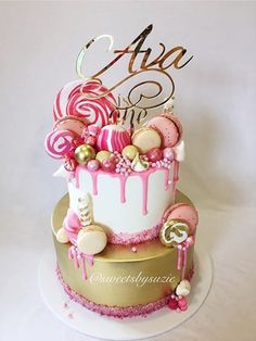 a pink and gold birthday cake with candy on the top is decorated with lollipops