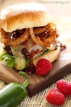 a chicken sandwich with raspberries on a cutting board next to some green peppers