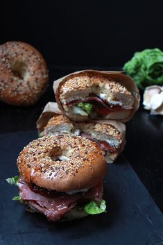 two bagels with meat, cheese and lettuce are on a black surface