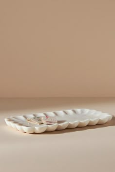 a small white plate with scalloped edges sits on a table against a beige background