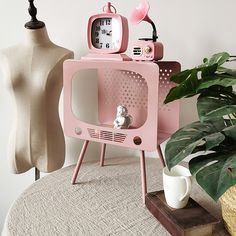 a pink tv set sitting on top of a table next to a potted plant