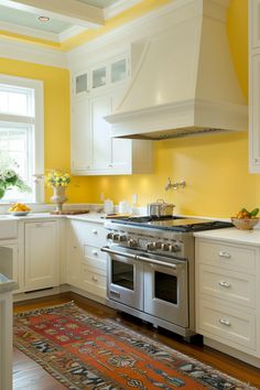 a kitchen with yellow walls, white cabinets and an area rug on the hardwood floor