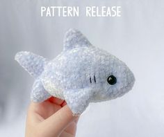 a hand holding a stuffed shark toy with the words pattern release on it's side