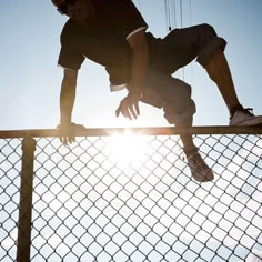 a man leaning on a fence with the sun behind him