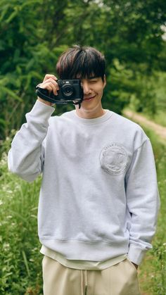 a young man holding up a camera to take a photo in front of some trees