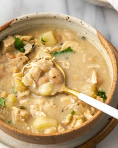 a bowl of chicken and dumpling soup with a spoon in it on a marble surface