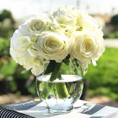 a vase filled with white flowers sitting on top of a table next to a book