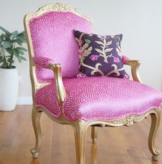 a pink chair sitting on top of a wooden floor next to a potted plant