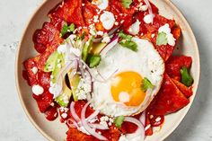 an egg is sitting on top of a plate of mexican food with onions, avocado and sour cream