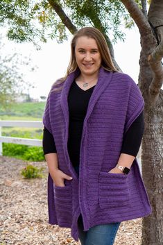 a woman standing in front of a tree wearing a purple knitted cardigan sweater