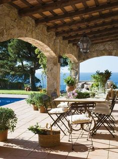 an outdoor dining table with chairs and potted plants next to a swimming pool in the background