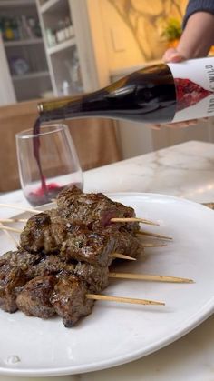 a plate with skewered meat on it and a glass of wine in the background