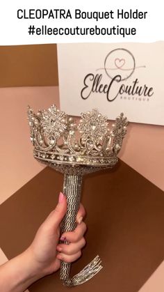 a woman holding a large silver crown on top of a brown table next to a sign that says cleopatra boutique