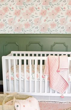 a white crib with pink and green floral wallpaper next to it, in front of a baby's bed