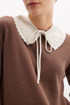 a woman wearing a brown sweater with a white collar and lace detail on the neck