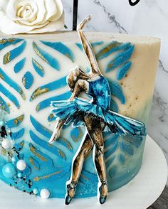 there is a blue and white cake with a ballerina figure on the front, and a rose in the back