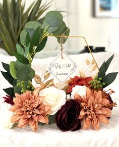 an arrangement of flowers and greenery on a white bed with a name tag attached to it