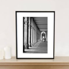 a black and white photo hanging on a wall above a mantle with two candles next to it