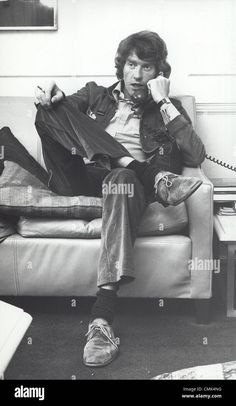 an old black and white photo of a man sitting on a couch talking on the phone