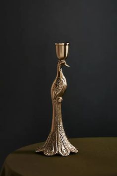 a gold colored candle holder with a bird on it's body and a green table cloth