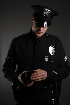 a police officer is looking at his cellphone while standing in front of a dark background